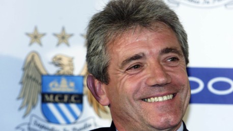 A man smiling at an event with a Manchester City crest in the background.