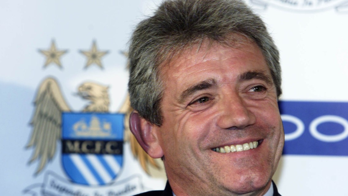 A man smiling at an event with a Manchester City crest in the background.