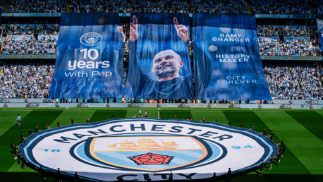 A large Manchester City banner celebrating 10 years with Pep displayed in a stadium, featuring slogans like 'Game Changer' and 'City Forever'.