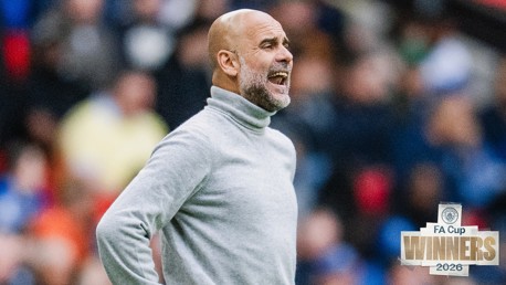 A man in a grey turtleneck stands on the sidelines with a blurred face. Text on the image reads 'FA Cup WINNERS 2026' next to a Manchester City logo.